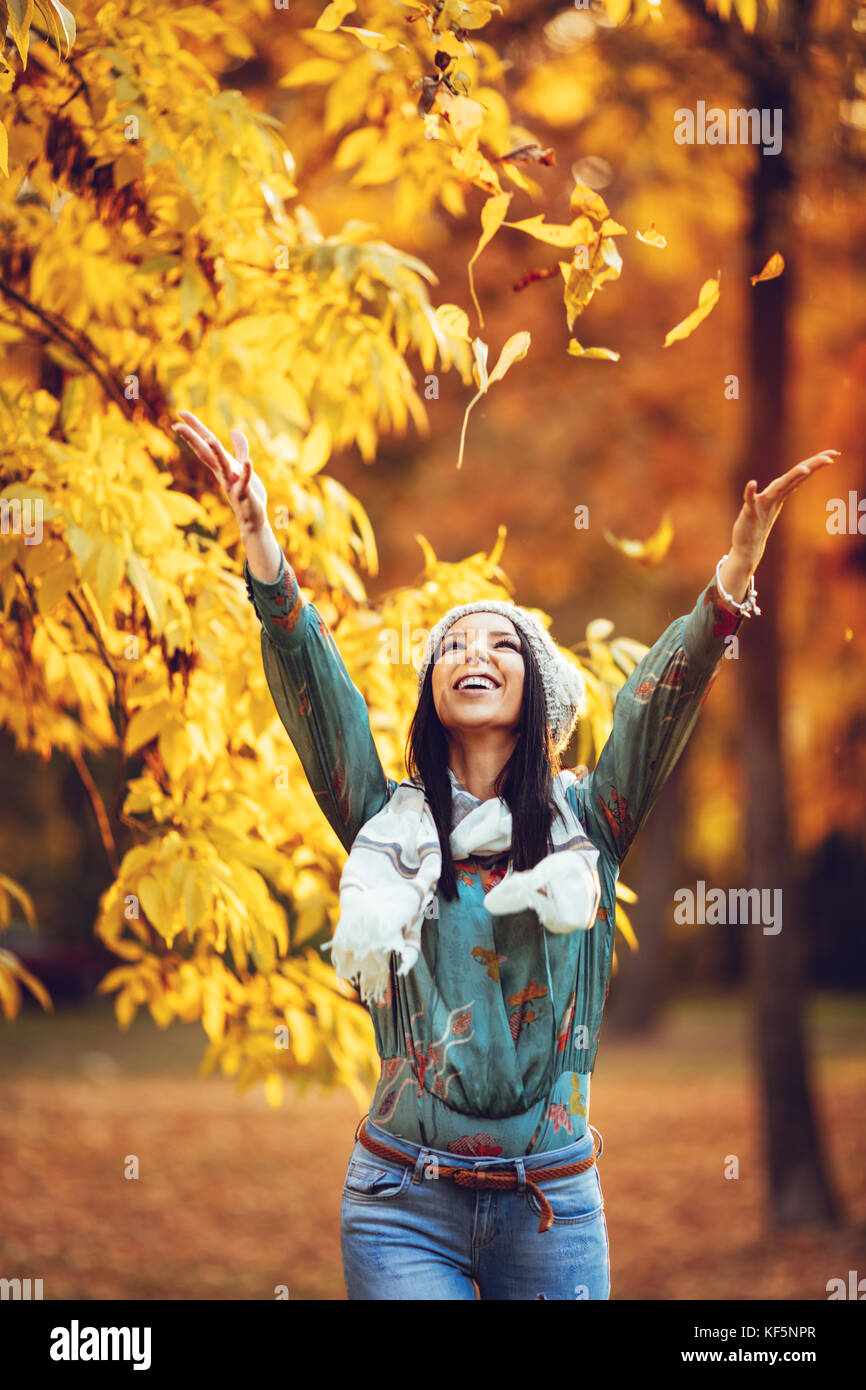 Cheerful young Beautiful woman aller seul dans le parc et se jette dans les feuilles d'automne ensoleillée d'or. Banque D'Images