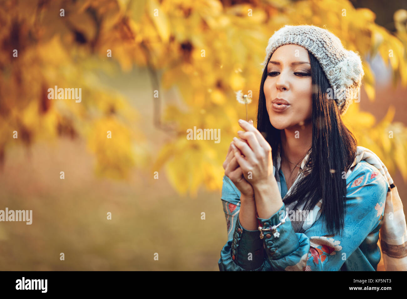 Portrait of young beautiful smiling positive young woman blowing dandelion in autumn park. Banque D'Images