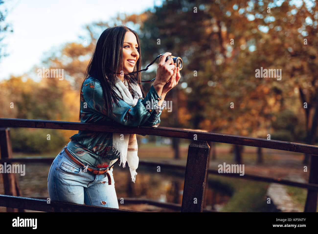 Femme photographe professionnel détenant un appareil photo numérique et la prise de photo sur le pont en automne parc de la ville. Banque D'Images