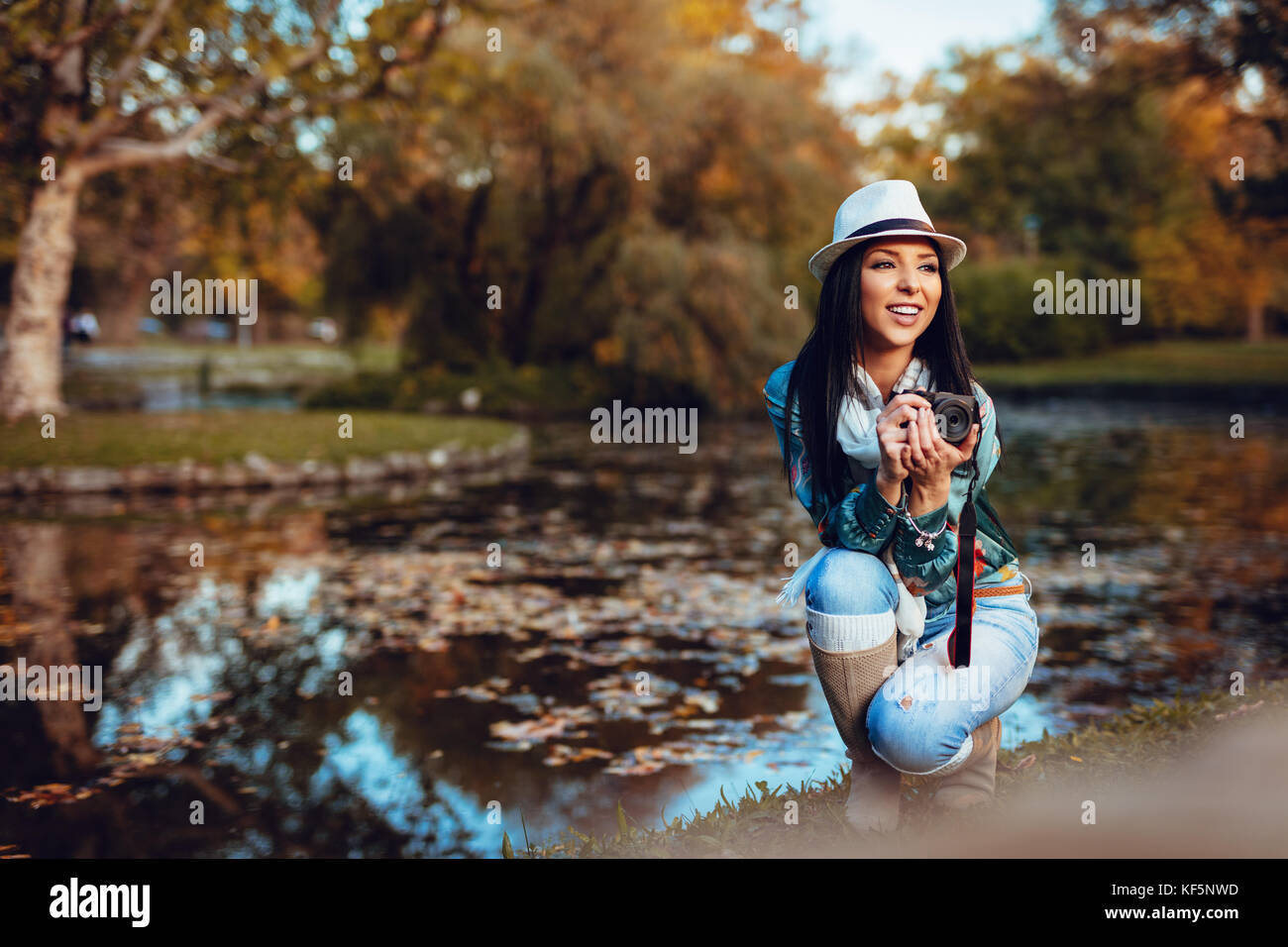 Happy woman holding photographe appareil photo numérique professionnel et taking photo près du lac, dans le parc de l'automne. Banque D'Images