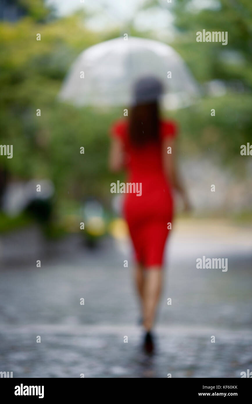 Hors focus portrait de l'arrière d'une femme dans une élégante robe rouge avec un parapluie de marche sous la pluie sur une ville rue pavée Banque D'Images