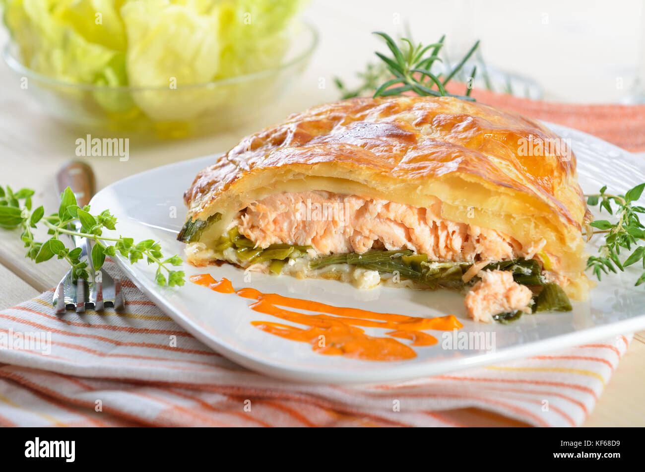 Filet de saumon sur les poireaux, cuit en pâte feuilletée, servi avec des fines herbes, sauce et salade Banque D'Images
