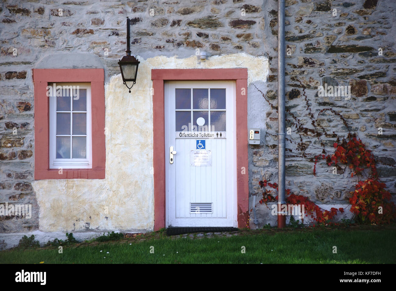 Des toilettes publiques dans un cottage nostalgique d'une façade en pierre et d'une lanterne. Banque D'Images