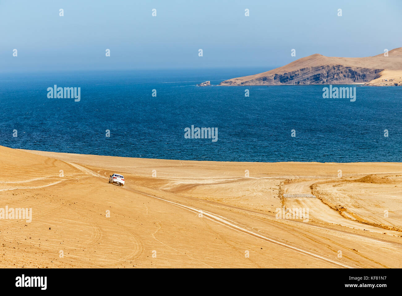 Voiture blanche de la conduite dans le désert de paracas vers les eaux bleues de l'océan pacifique, Paracas, Pérou Banque D'Images