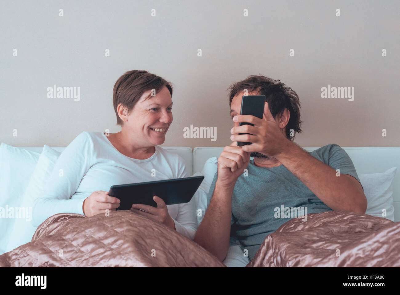 Heureux couple, mari et femme dans la chambre à l'aide d'appareils électroniques personnels Banque D'Images