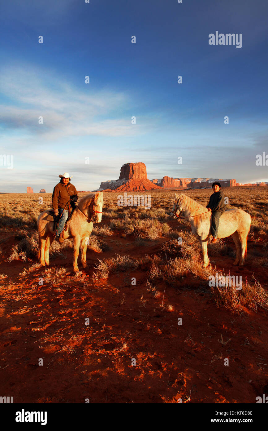 Usa ; Arizona ;, Monument Valley Navajo Tribal Park, un homme navajo et son fils monter à cheval avec Mitchell butte et mitchell mesa dans la distance Banque D'Images