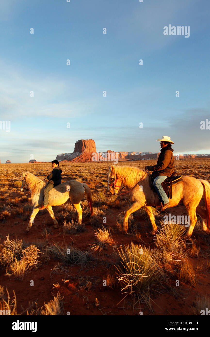 Usa ; Arizona ;, Monument Valley Navajo Tribal Park, un homme navajo et son fils monter à cheval avec Mitchell butte et mitchell mesa dans la distance Banque D'Images