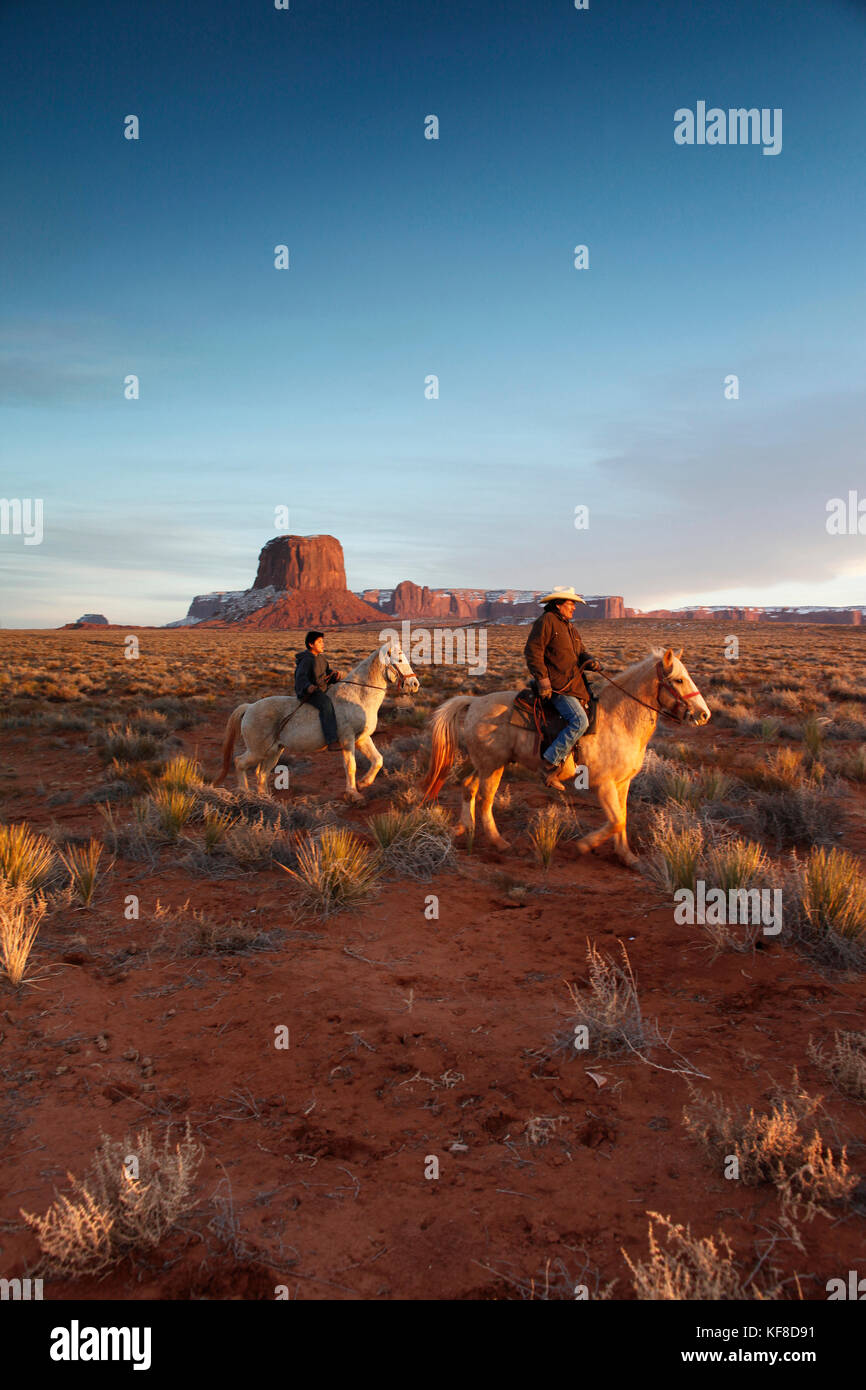 Usa ; Arizona ;, Monument Valley Navajo Tribal Park, un homme navajo et son fils monter à cheval avec Mitchell butte et mitchell mesa dans la distance Banque D'Images
