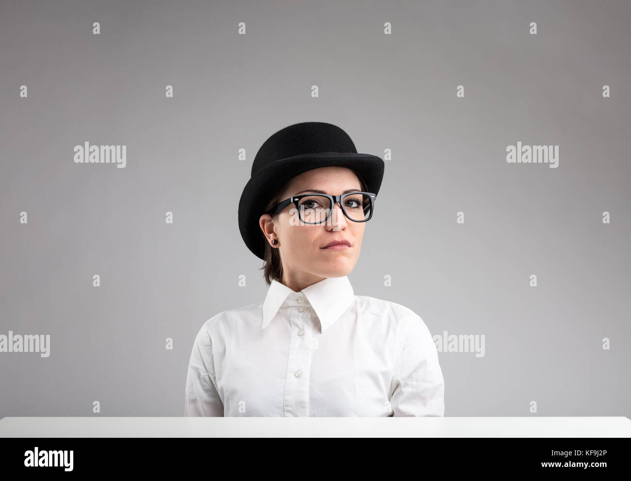 Stern woman in bowler, verres, et chemise blanche sur fond gris Banque D'Images