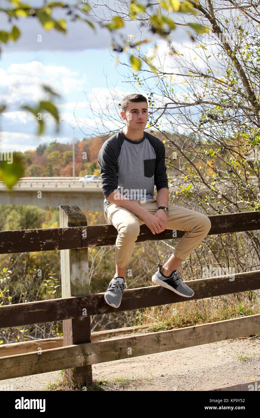Adolescent garçon assis sur une barrière à la reflective Banque D'Images
