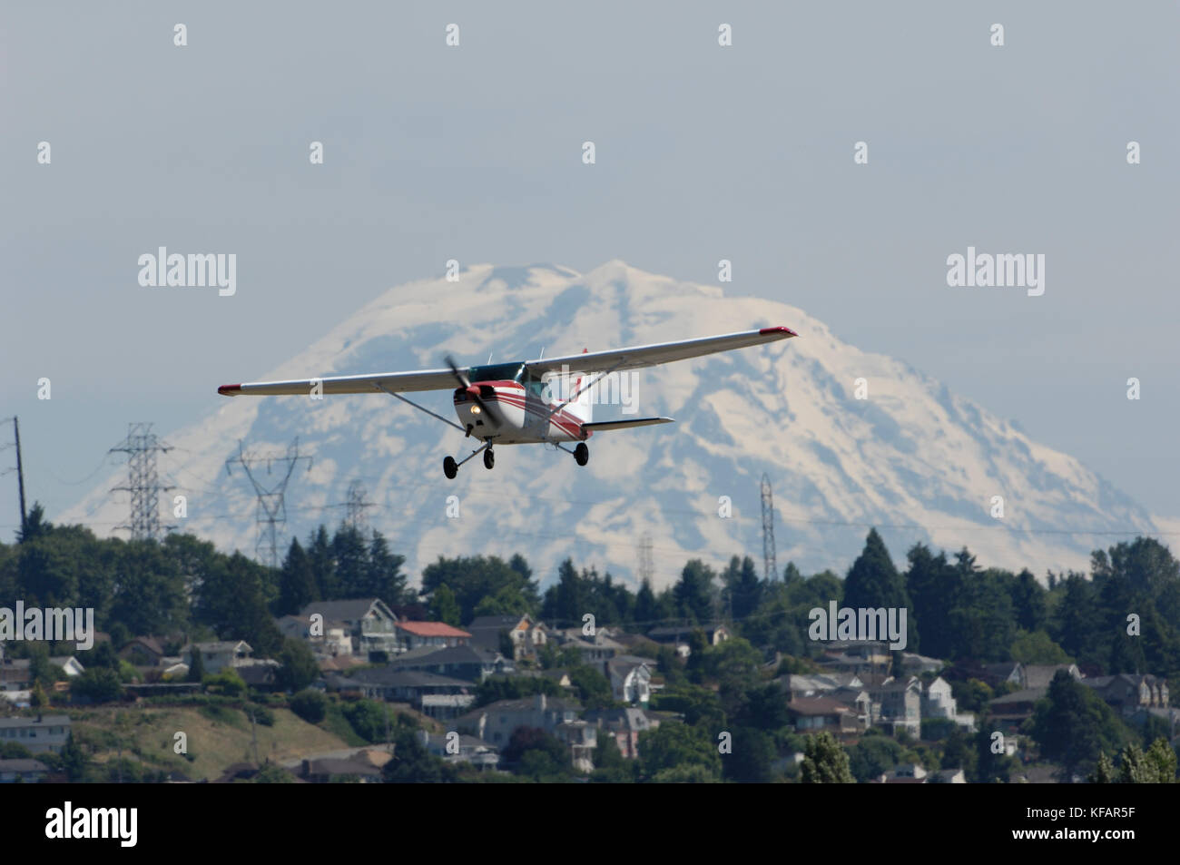 Un Cessna 172N Skyhawk le décollage avec le Mont Rainier, arbres, maisons et pylônes derrière Banque D'Images