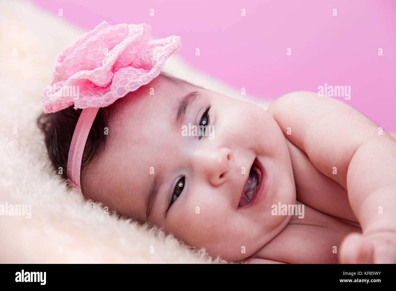 Mignon, joli, heureux, chubby portrait de fille de bébé avec un grand sourire, riant. Nu ou nu sur une couverture moelleuse. Serre-tête à fleurs roses. Bébé de quatre mois Banque D'Images