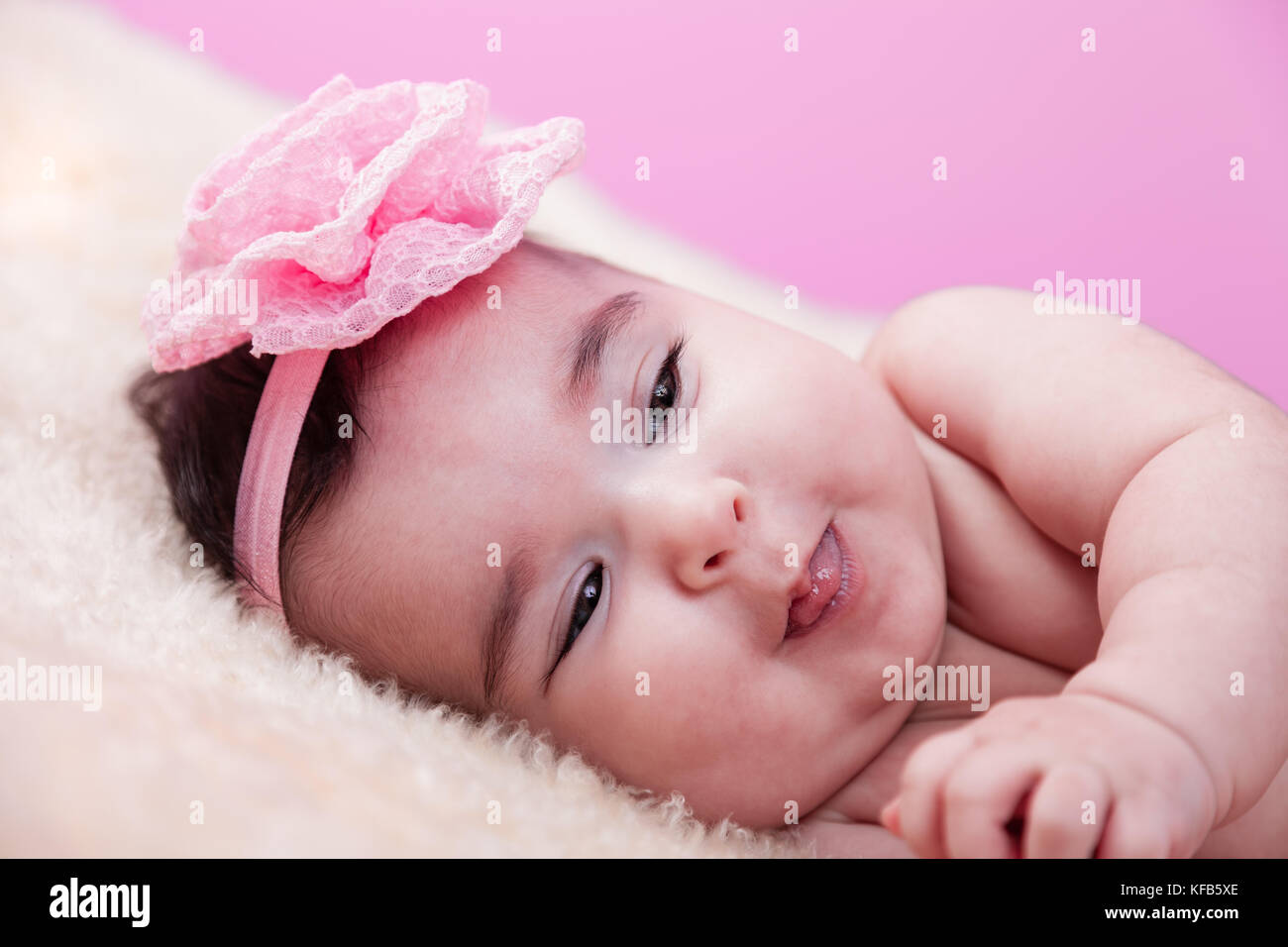 Mignon, joli, heureux, chubby portrait de bébé fille souriant et joueur de la langue. Nu ou nu sur une couverture moelleuse. Serre-tête à fleurs roses. Quatre mois Banque D'Images