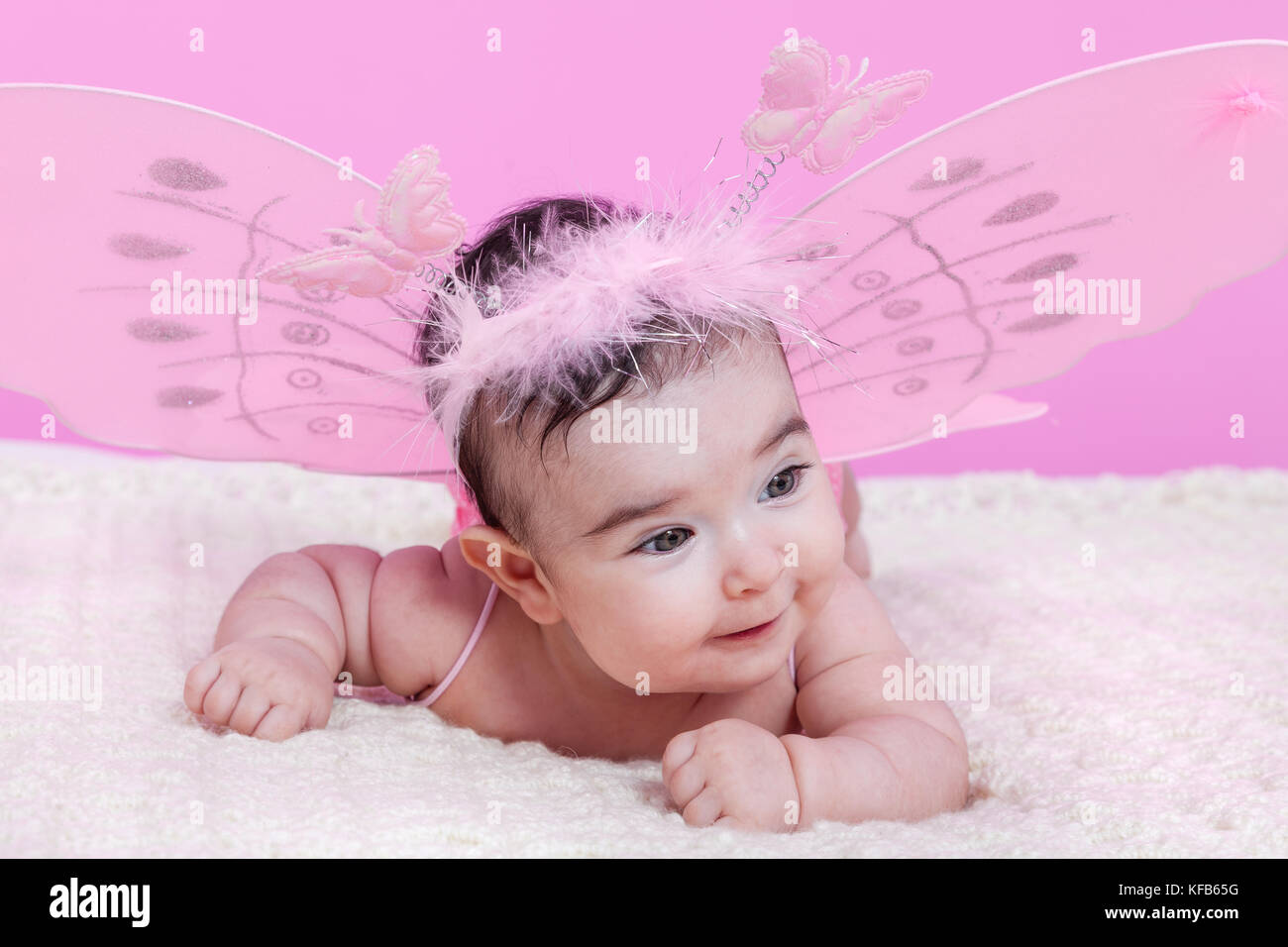 Petite fille mignonne, jolie, heureuse, souriante, avec des ailes de papillon roses et un serre-tête avec des papillons comme antennes. Quatre mois / bébé fille Banque D'Images
