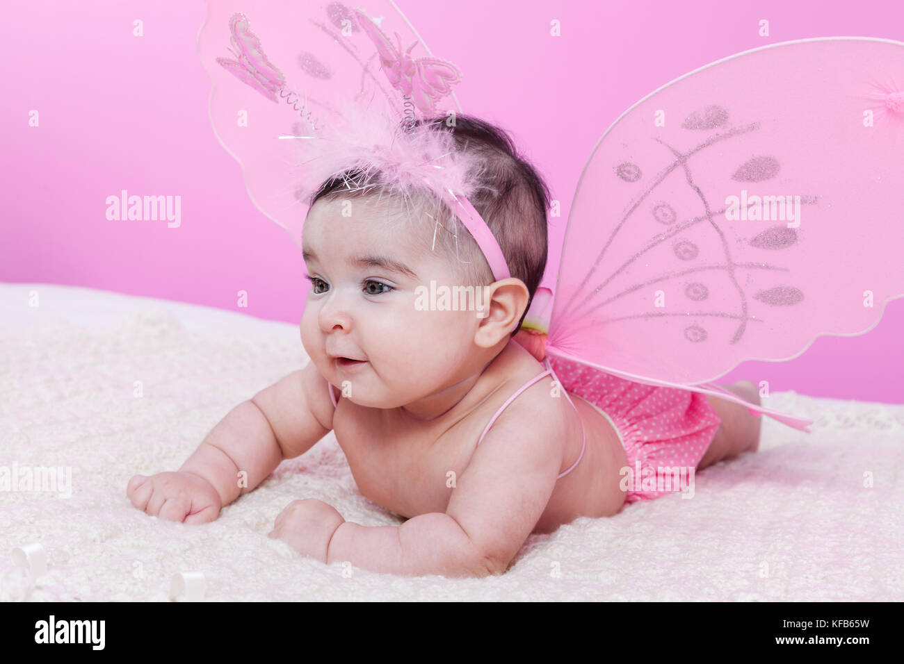 Petite fille mignonne, jolie, heureuse, souriante, avec des ailes de papillon roses et un serre-tête avec des papillons comme antennes. Quatre mois / bébé fille Banque D'Images