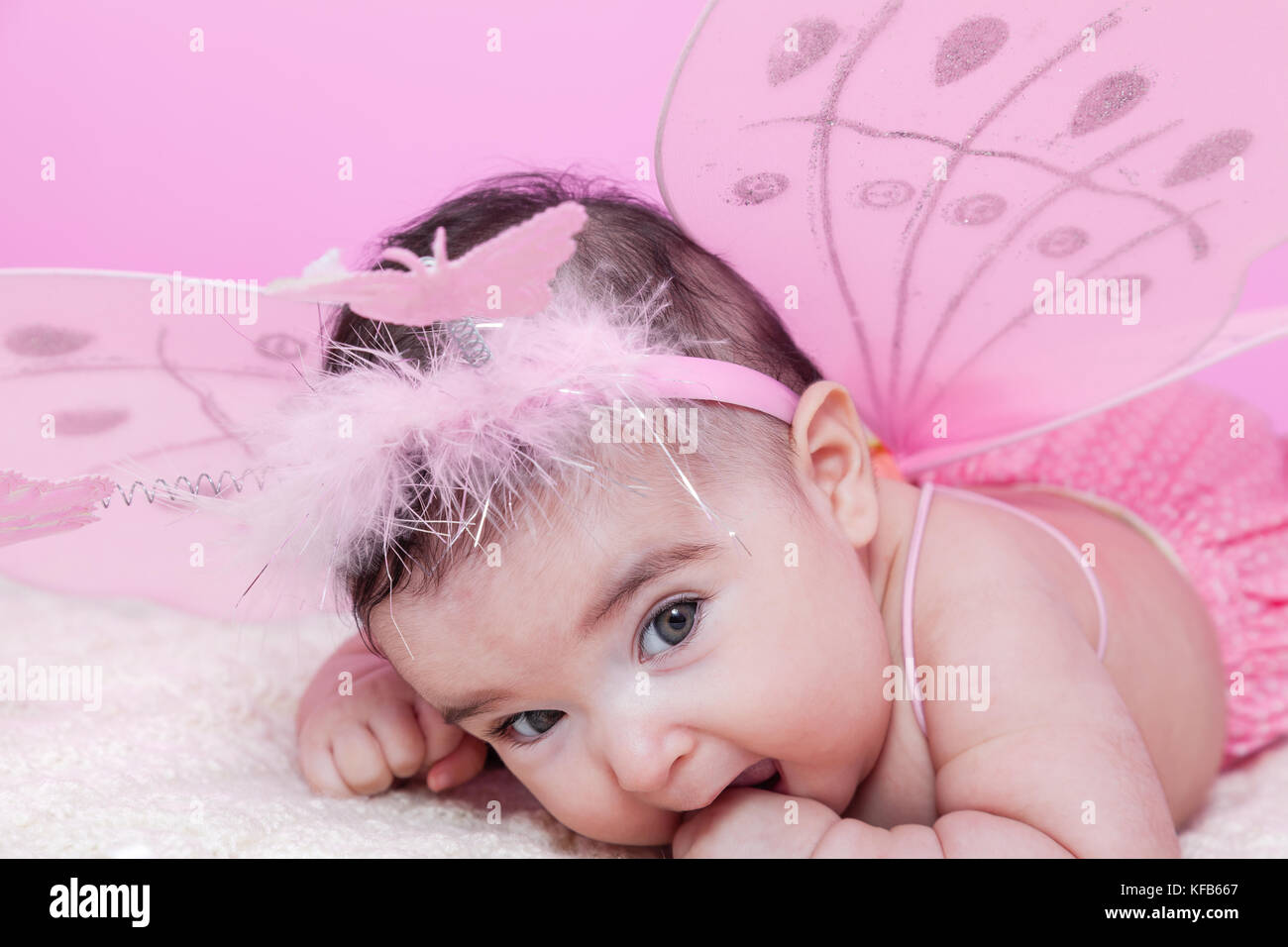 Joli, joli, heureux, chubby et souriant portrait de petite fille, avec des ailes de papillon roses et un serre-tête avec des papillons comme antennes. Bébé de quatre mois Banque D'Images