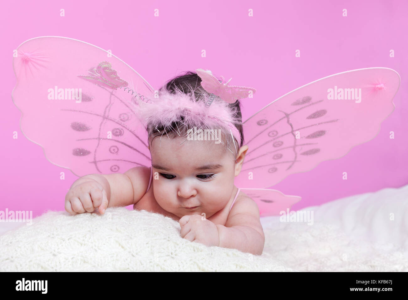 Mignon, joli, heureux, chubby bébé fille curieux au sujet des textures, avec des ailes de papillon roses et serre-tête avec des papillons comme antennes. Quatre mois Banque D'Images