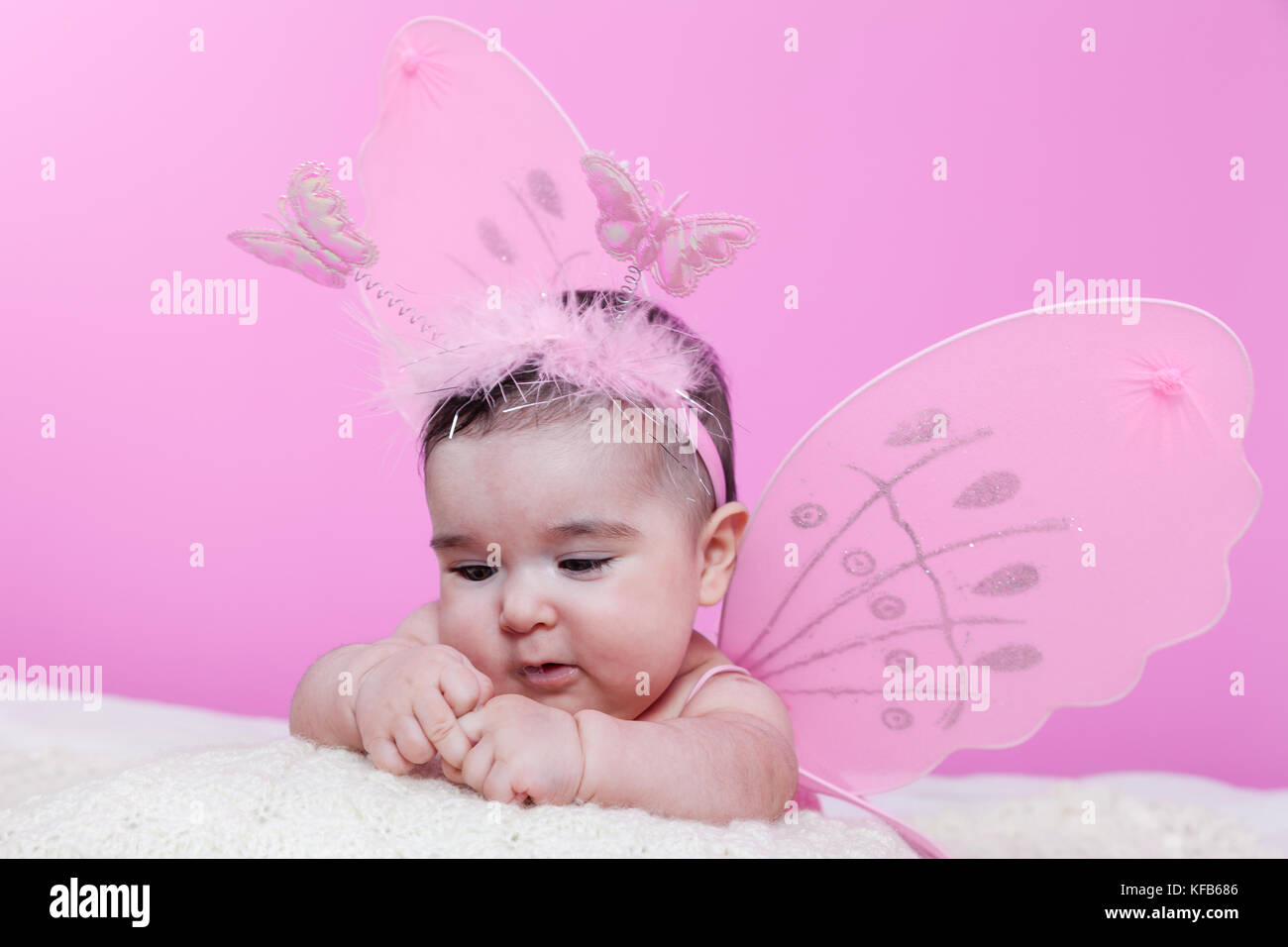 Mignon, joli, heureuse, fille de bébé joufflu curieux au sujet de ses mains, avec les ailes de papillon rose et serre-tête avec des antennes comme les papillons. 4 mois Banque D'Images