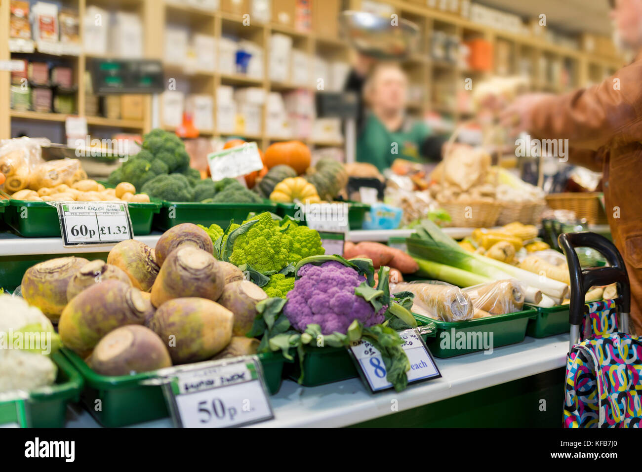 Close up of delicious et légumes colorés avec l'échoppe de marché et commerçant du marché de plus en plus floue dans l'arrière-plan qui sert un client en Angleterre, Royaume-Uni Banque D'Images