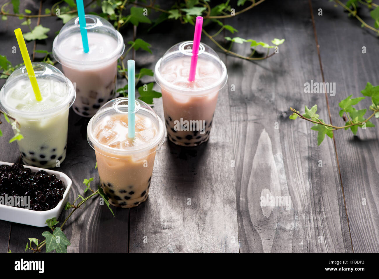 Variété de bubble tea dans des gobelets en plastique avec paille sur une table en bois. Banque D'Images