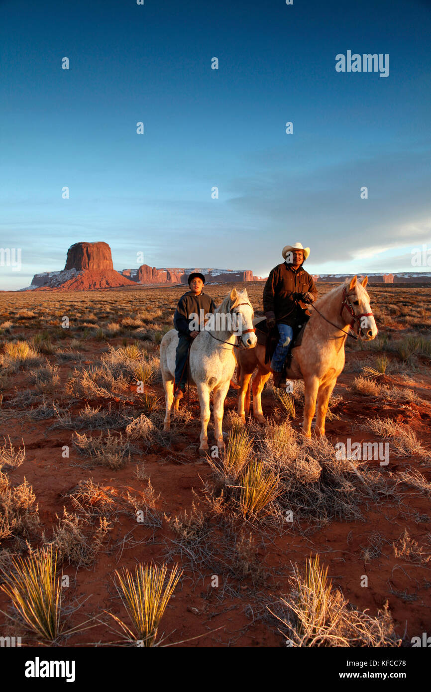 Usa ; Arizona ;, Monument Valley Navajo Tribal Park, un homme navajo et son fils monter à cheval avec Mitchell butte et mitchell mesa dans la distance Banque D'Images