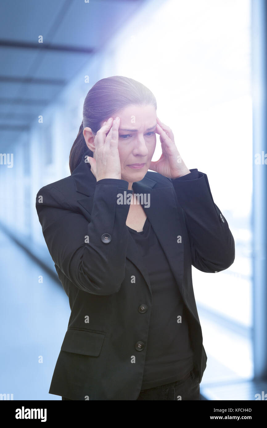 Femme d'âge moyen avec syndrome de douleur chronique fibromyalgie souffrant de une crise de migraine aiguë à son bureau Banque D'Images