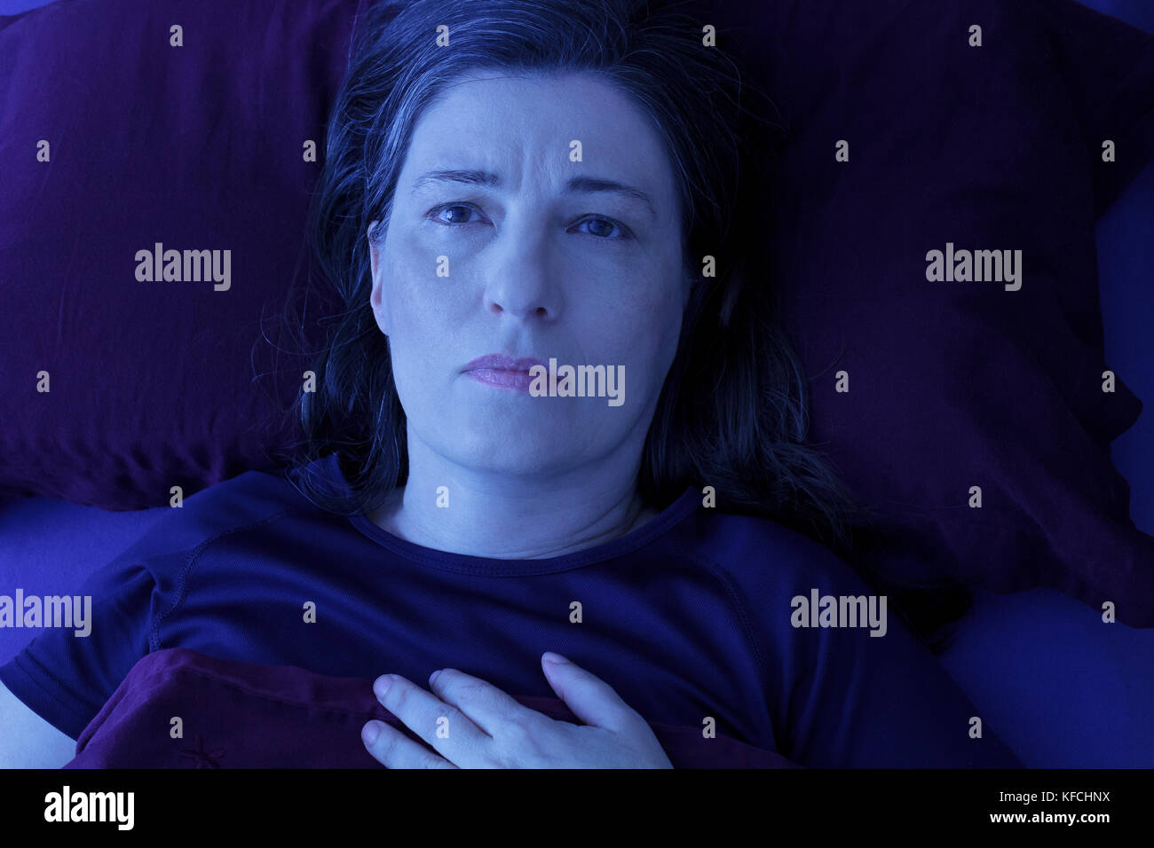 Middle aged woman lying awake dans son lit la nuit à cause de l'insomnie, le stress, les peurs, les cauchemars ou le syndrome des jambes Banque D'Images