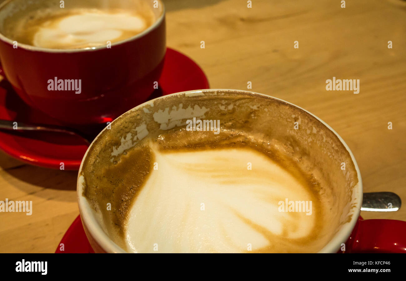 Gros plan d'un café latte en céramique rouge à moitié bu tasse et soucoupe sur une table en bois dans un café boutique Banque D'Images