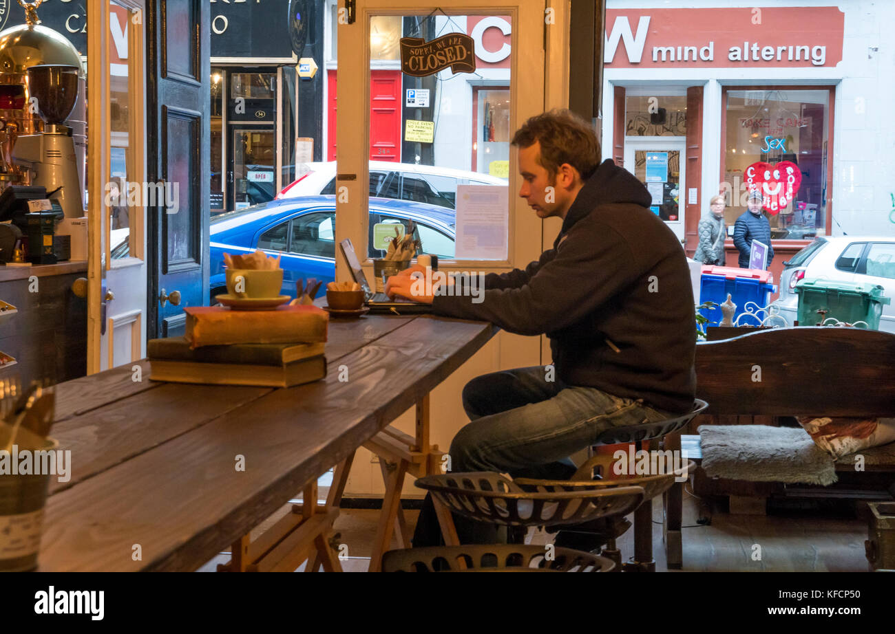 Jeune homme assis à table haute dans artisan café, Cockburn Street, Édimbourg, Écosse, Royaume-Uni, travaillant sur un ordinateur portable Banque D'Images