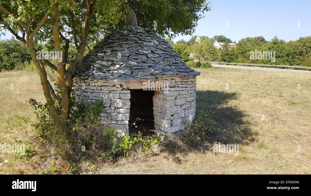 Construction en pierre d'Istrie entrée - structure kazun, entouré par de l'herbe sèche et de grands arbres sur une journée d'été Banque D'Images