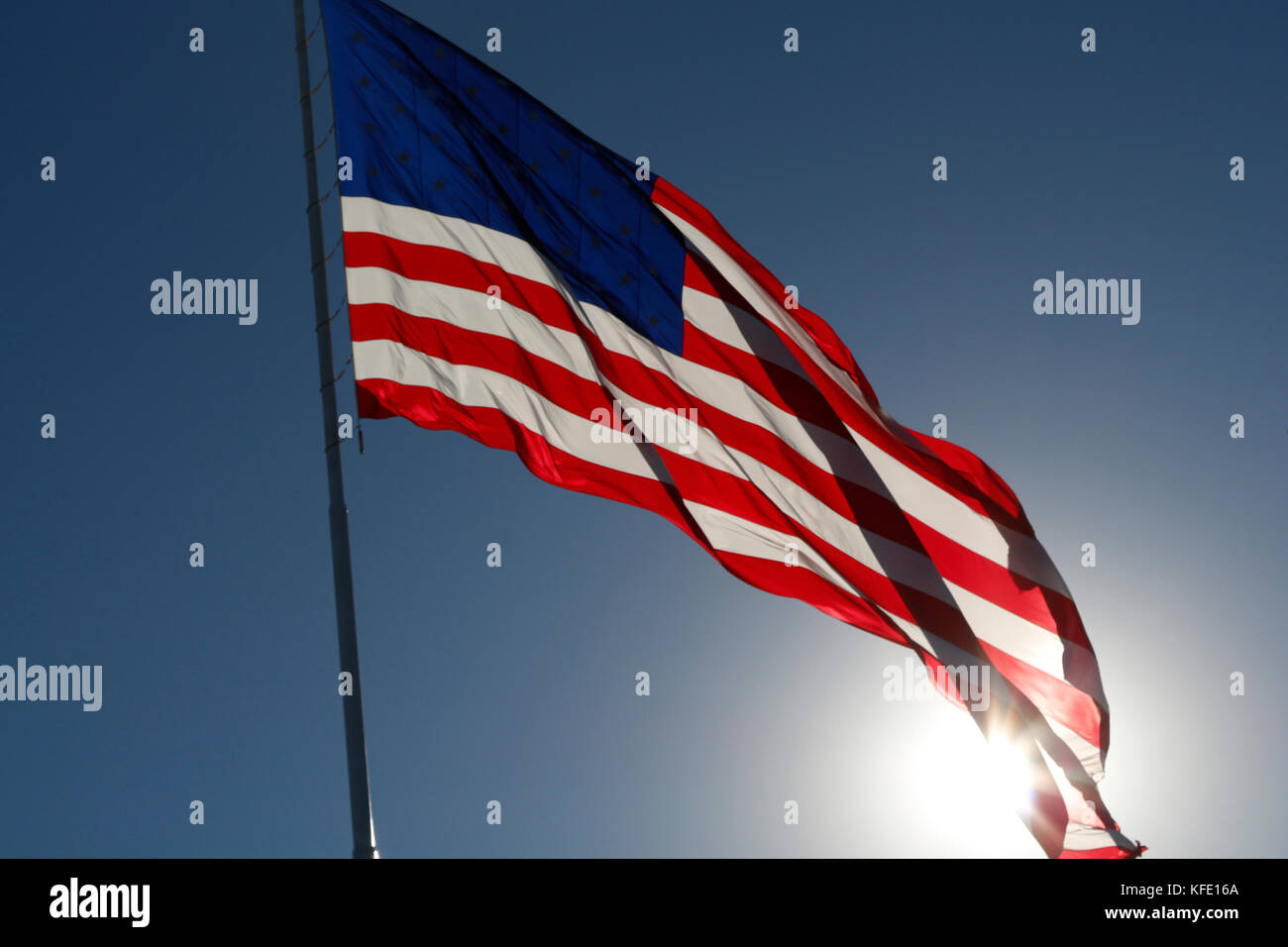 L'American flag flying fier contre le soleil dans un ciel bleu clair. Banque D'Images