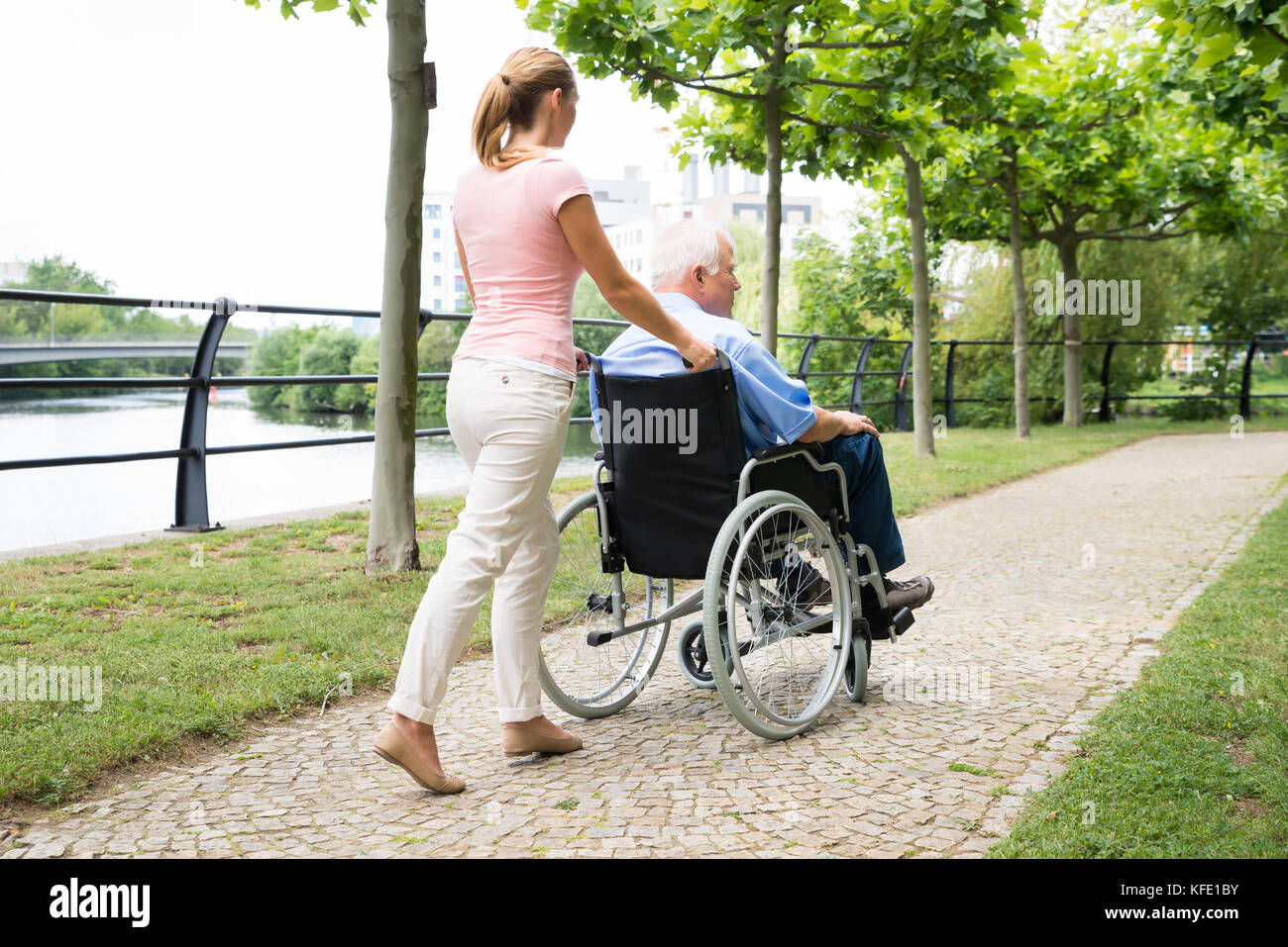 Vue latérale d'une jeune femme d'aider son père handicapé sur fauteuil roulant dans Park Banque D'Images