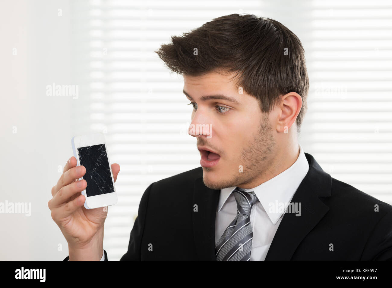 Malheureux jeune businessman looking at mobile phone in office cassé Banque D'Images