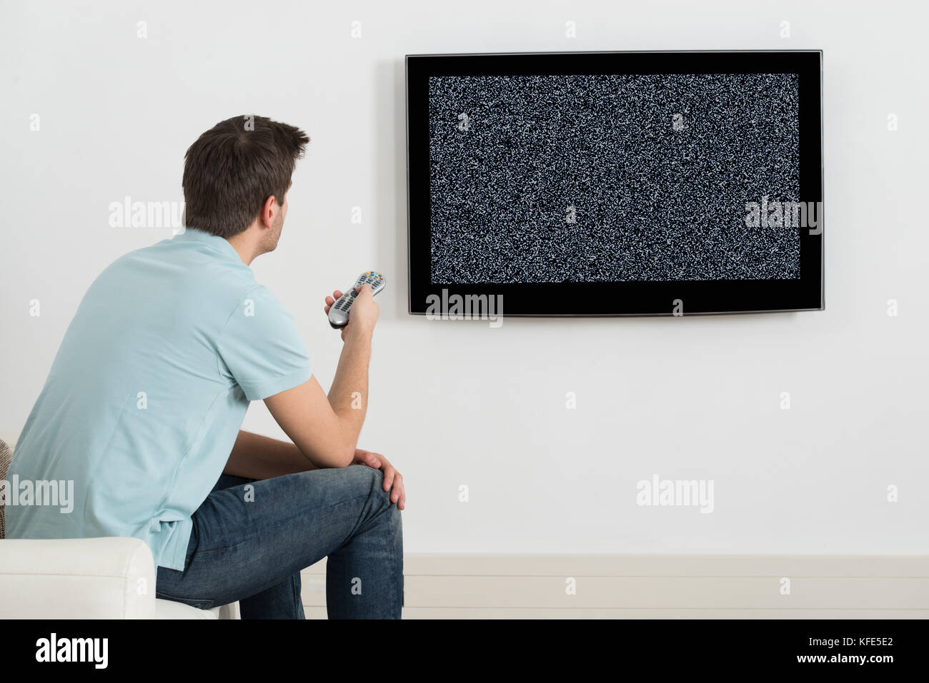 Homme assis sur le canapé devant la télévision avec aucun signal Banque D'Images