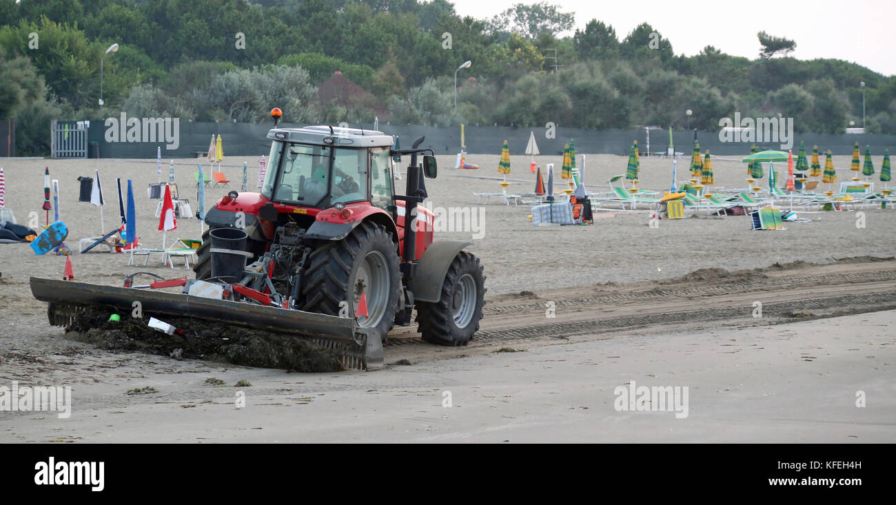 Un tracteur qui nettoie la plage à l'aube dans les déchets de la veille Banque D'Images