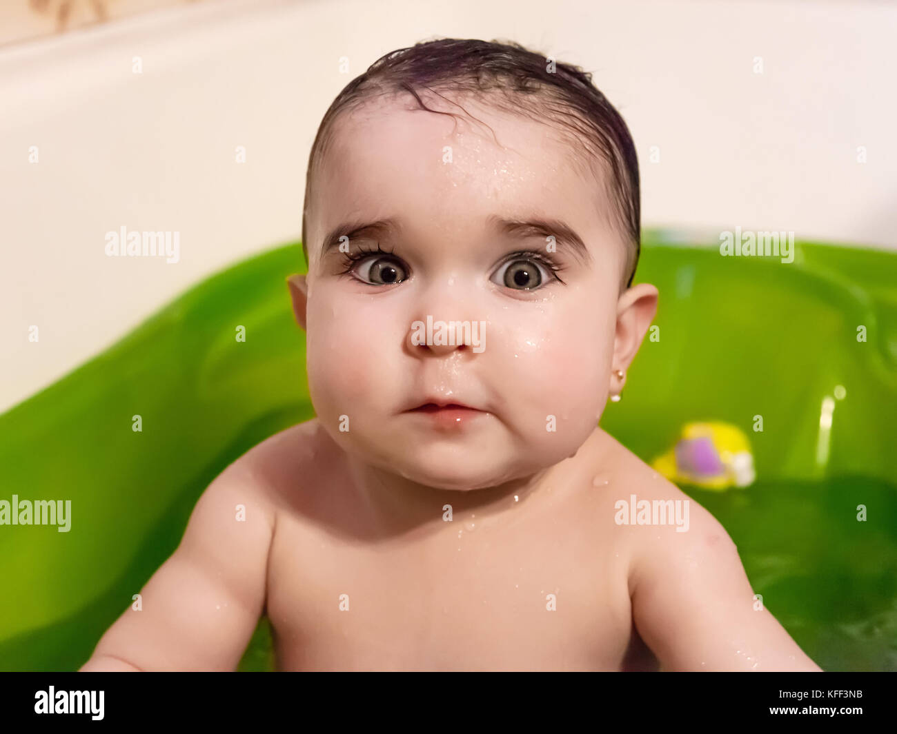 Mignon, joli, bébé fille de bain portrait avec l'expression surprise ou choquée. Mouiller les cheveux du bain dans une baignoire verte. Neuf mois / soins pour bébé Banque D'Images