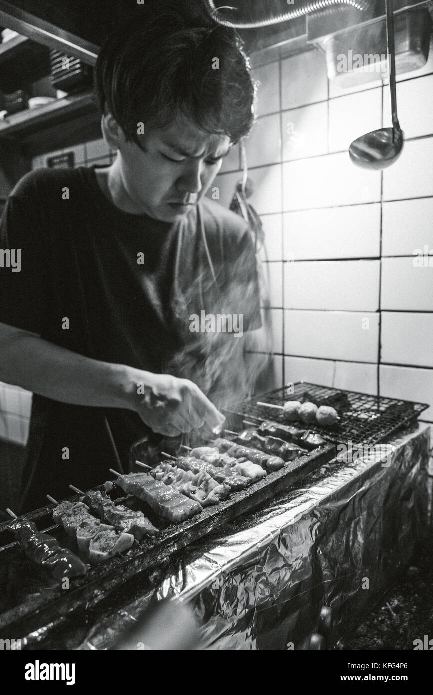 Jeune homme japonais prépare des brochettes yakitori. Banque D'Images