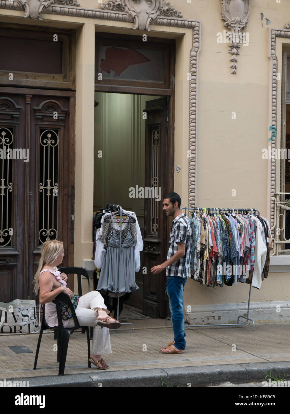 Jeune homme et femme sur trottoir en face de l'ancien bâtiment de discuter avec la mode des vêtements de racks dans et à côté de la porte. Bois et ornés de porte en laiton Banque D'Images