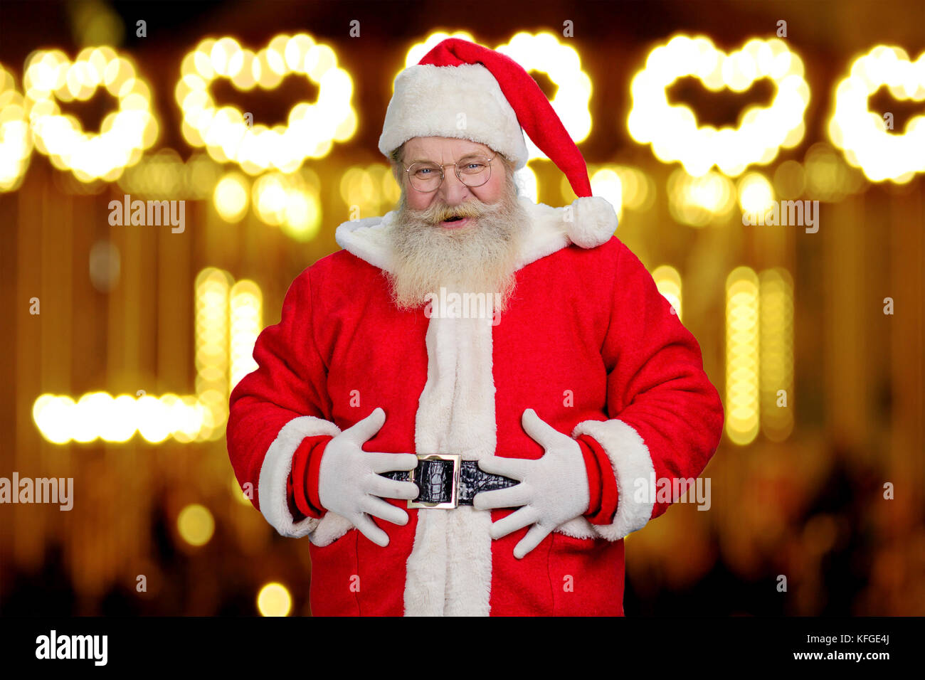 Portrait du père Noël avec les mains sur le ventre. smiling foi père Noël avec les mains de courroie, nouvelle année lumières fond. Banque D'Images