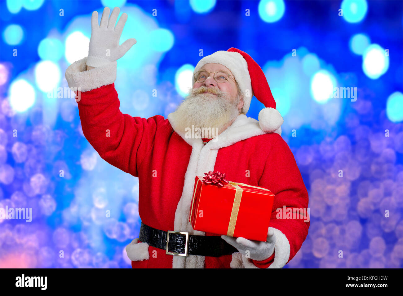 Portrait du père Noël à la hausse. heureux père noël avec boîte-cadeau, et l'agitant avec la main, bleu fond brillant. Banque D'Images