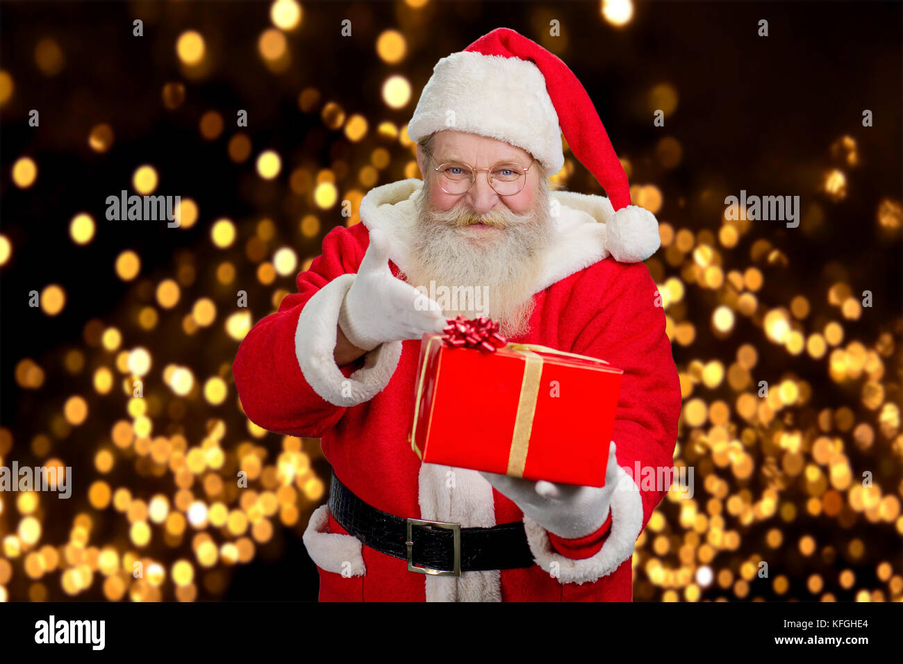 Heureux père noël offrant présents. genre père noël avec boîte cadeau rouge sur fond lumières de fête. Banque D'Images