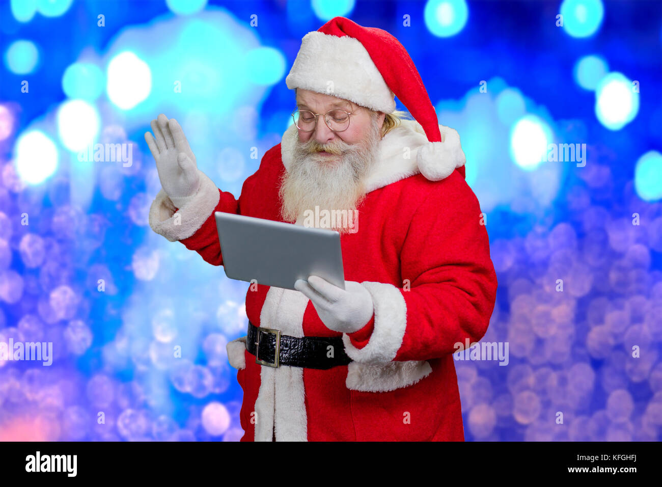 Surpris le père Noël avec le PC tablette. hauts santa claus holding tablet ordinateur et main levée, bleu fond de fête. Banque D'Images