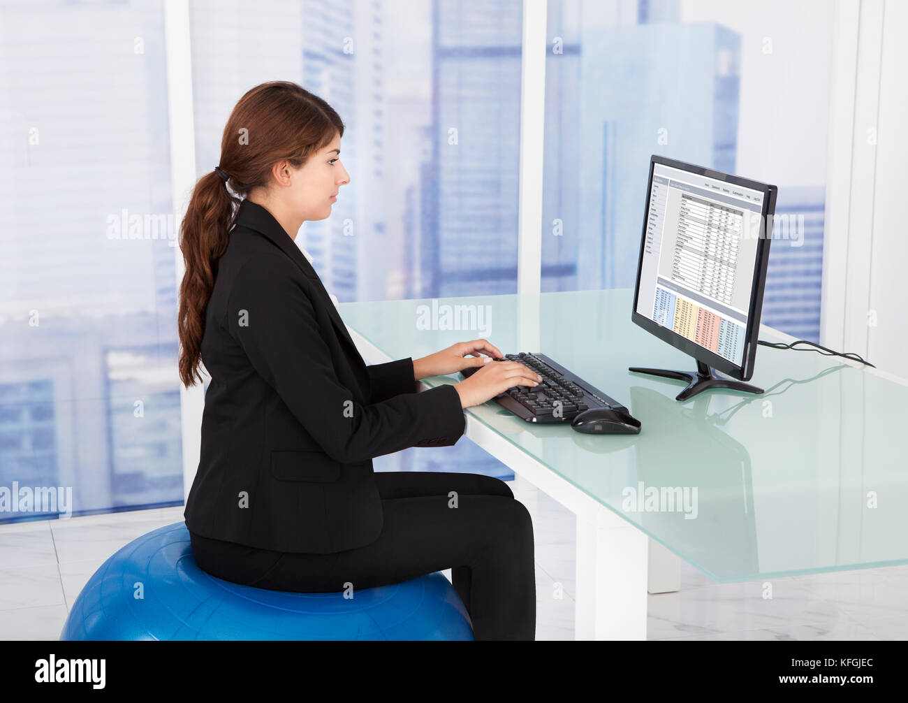Vue de côté businesswoman using computer while sitting on fitness ball at desk in office Banque D'Images