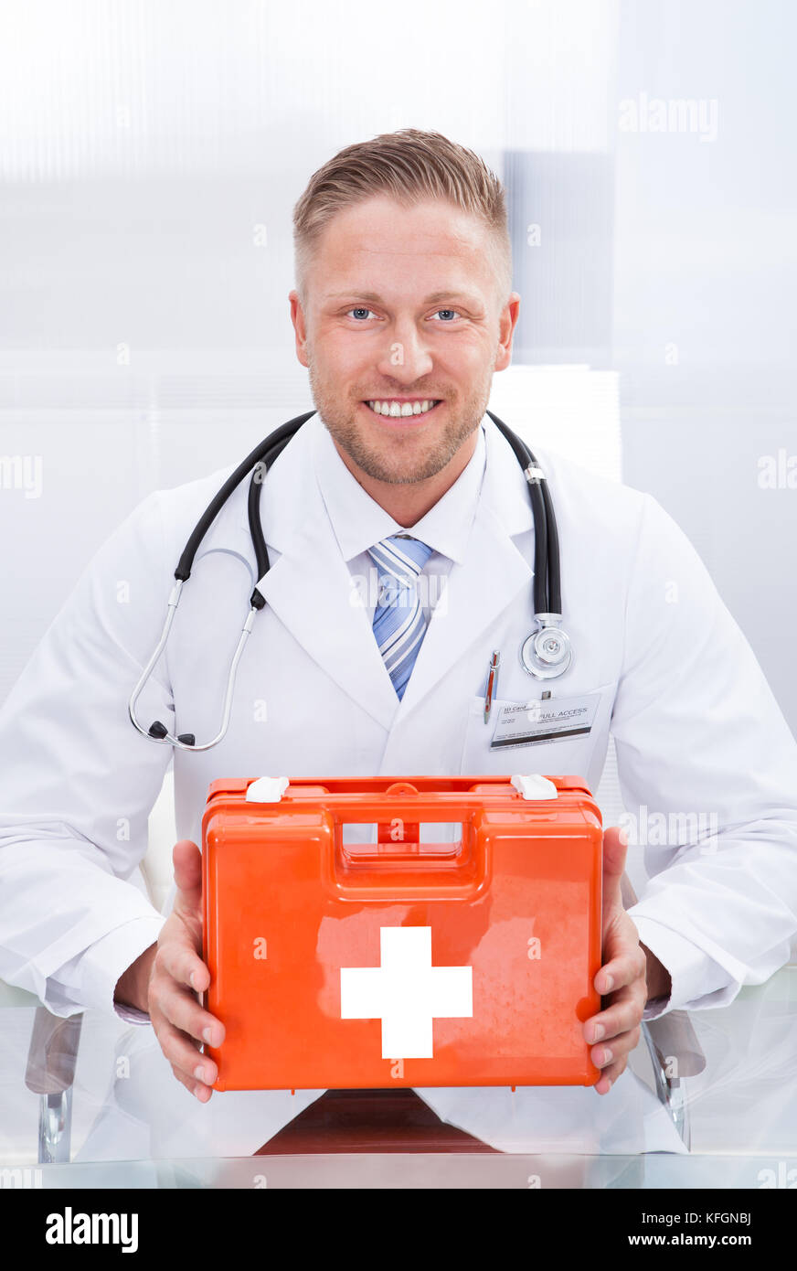 Smiling doctor ou du personnel paramédical dans un sarrau blanc avec un stéthoscope autour du cou, tenant une boîte rouge contenant une trousse de premiers soins Banque D'Images