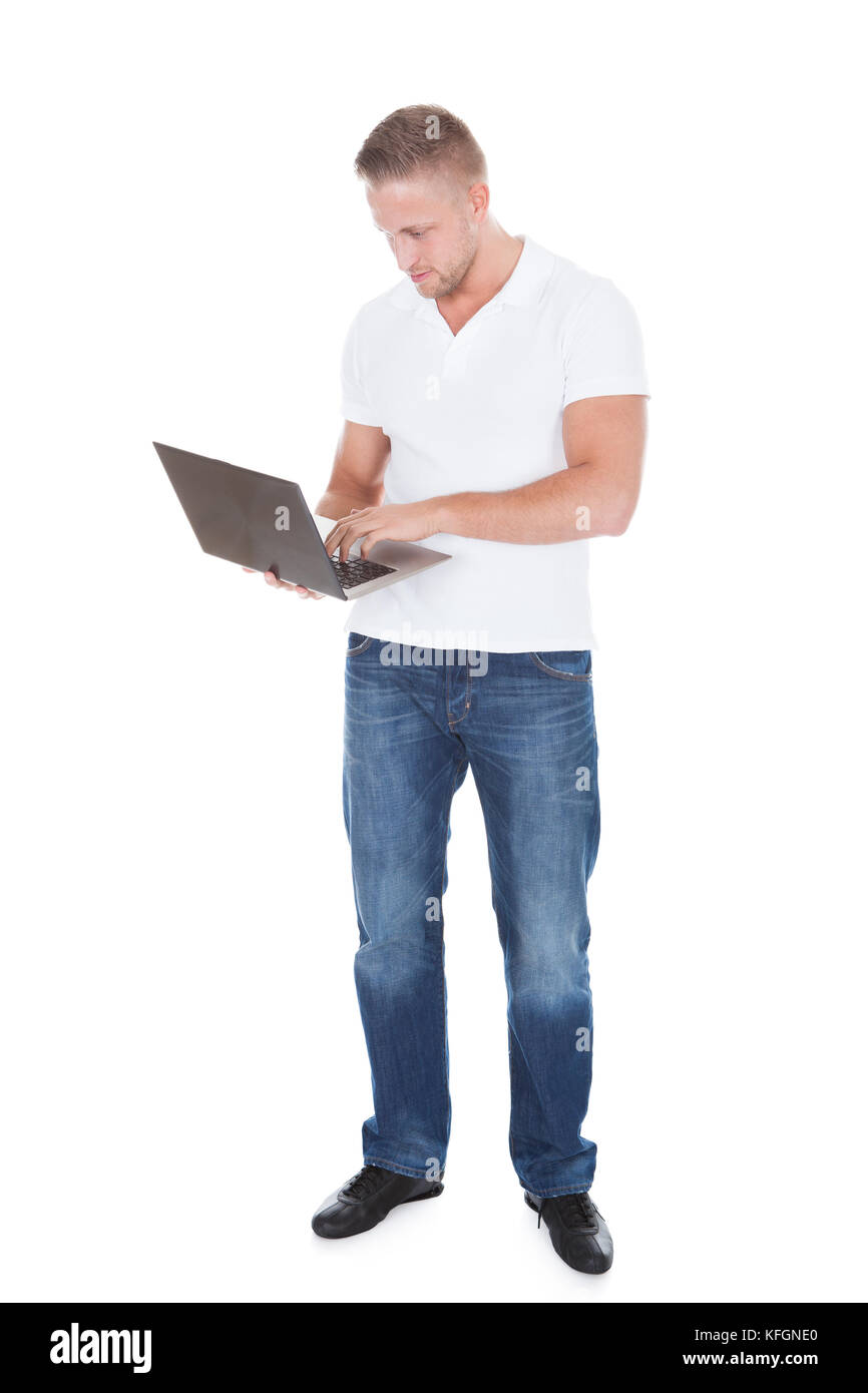 Smiling man en jeans à l'aide d'un permanent de poche ordinateur portable en équilibre sur sa paume qu'il regarde la caméra avec un sourire amical isolated on white Banque D'Images
