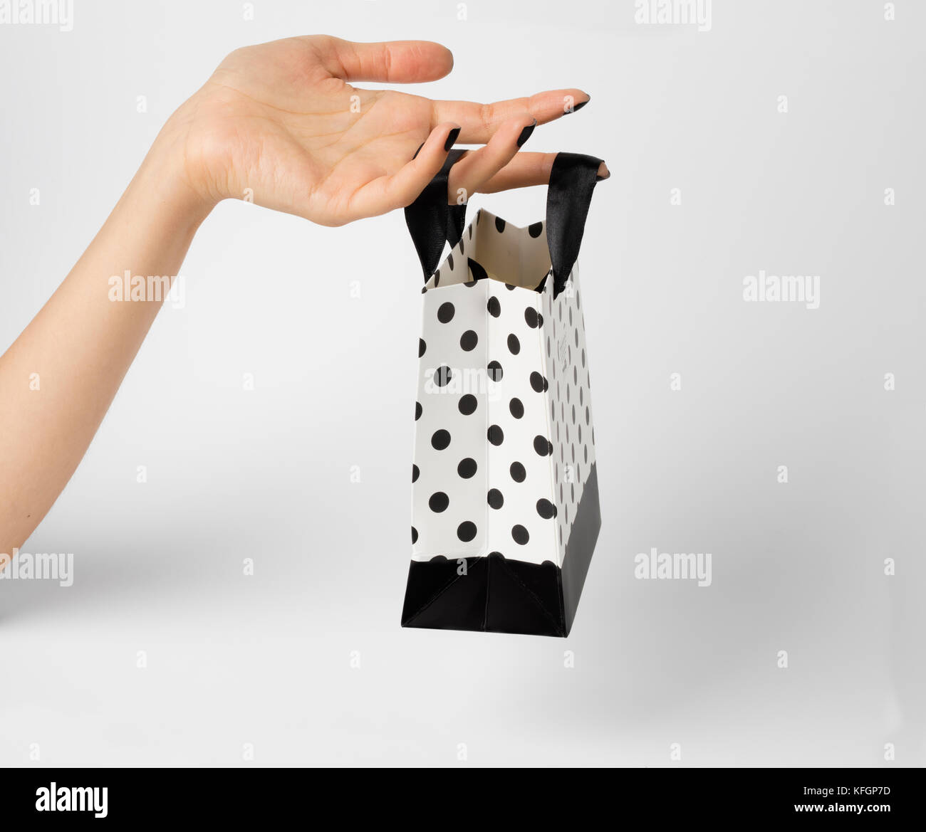 La tenue d'une main de femme sac cadeau blanc, à pois blancs sur fond blanc.. Banque D'Images
