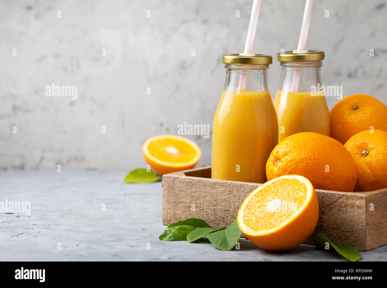 Le jus d'orange dans des bouteilles en verre, les oranges fraîches dans un plateau en bois (fort) sur un fond de béton gris Banque D'Images