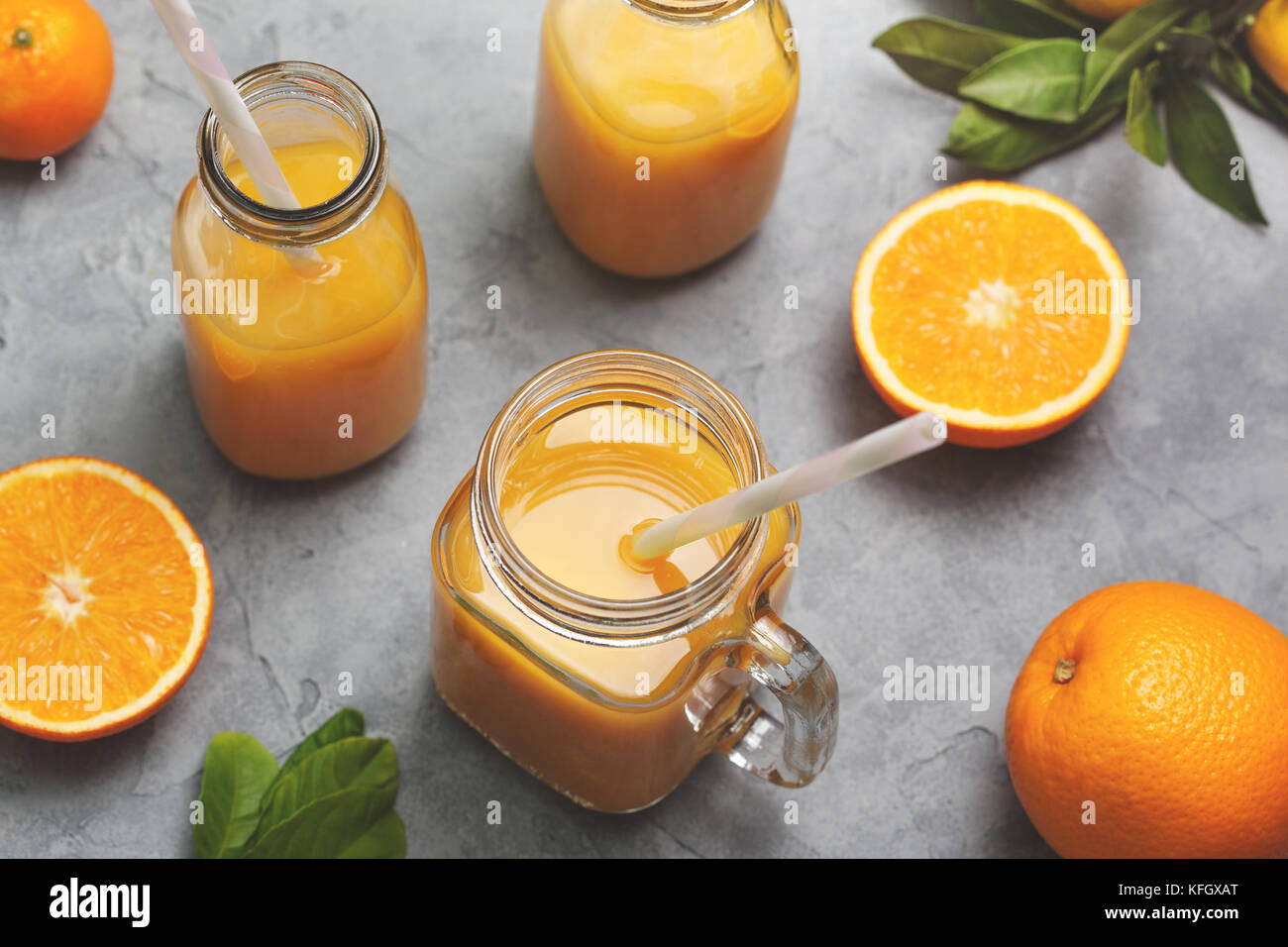 Le jus d'orange dans un pot Mason, bouteilles en verre, les oranges fraîches sur un fond de béton gris. Vue de dessus. selective focus Banque D'Images