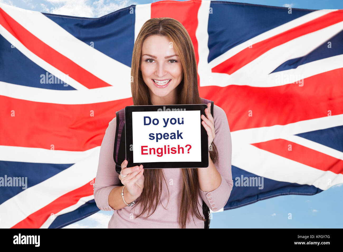 Jeune femme tenant une tablette numérique demandant parlez-vous anglais devant le drapeau britannique Banque D'Images