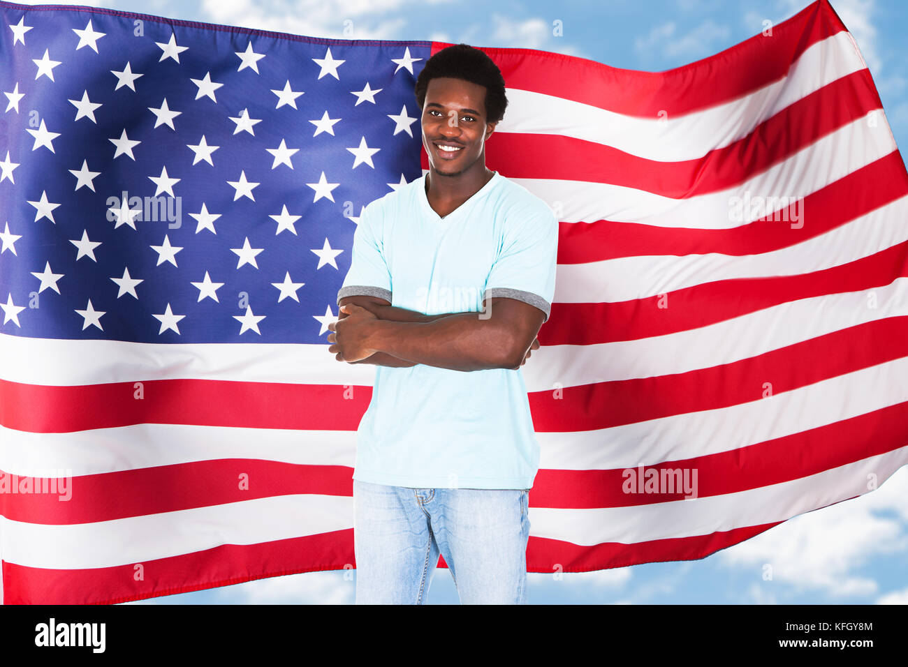 Jeune homme africain souriant avec bras croisé devant le drapeau des États-Unis Banque D'Images